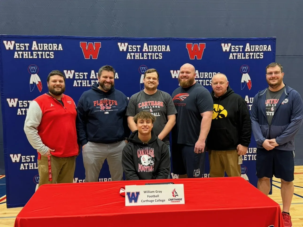 Will seated at the signing table with six of his coaches standing behind him