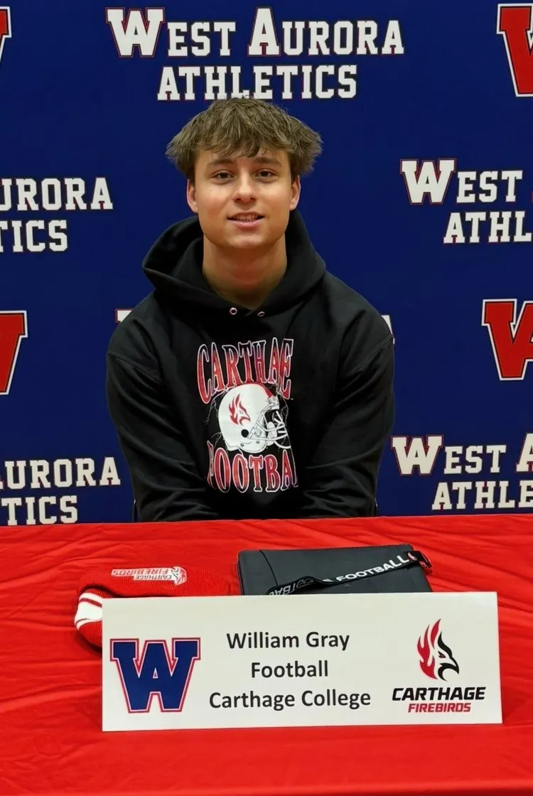 Will seated at the West Aurora signing table in a Carthage Football hoodie, behind his name card