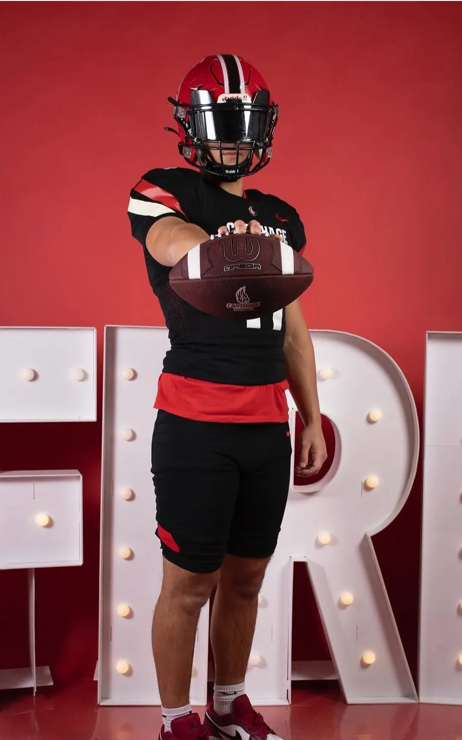 Will holding a football out toward the camera in a black Carthage jersey
